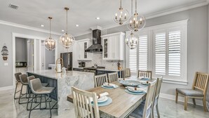 A spacious kitchen with a marble island, wooden chairs, and pendant lighting.