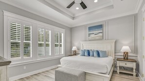 A bedroom with a large bed, two bedside tables with lamps, a bench, and a ceiling fan.