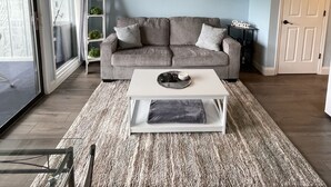 A living room with a gray sofa, a white coffee table, a ceiling fan, and a painting of sailboats.