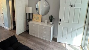 A living room with a black sofa, a white dresser with drawers, a round mirror, and a door labeled 403.