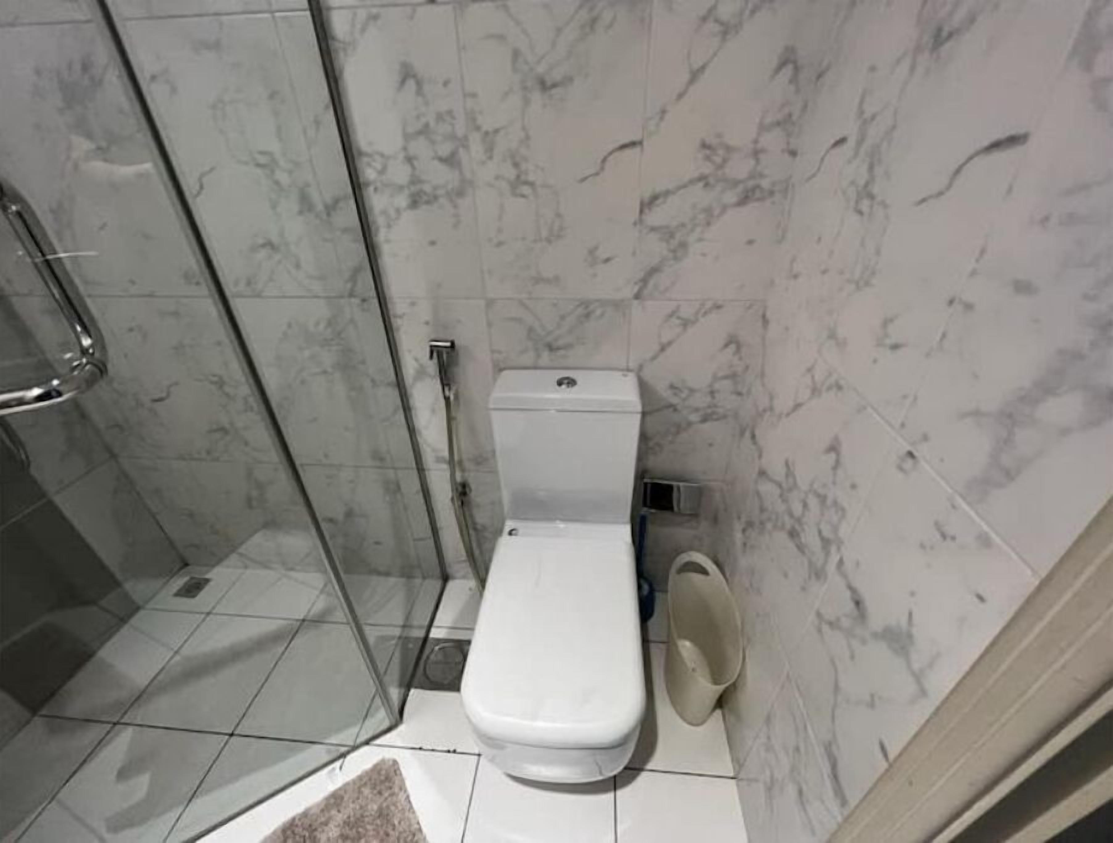 Une salle de bain comprenant des toilettes, une douche en verre et un mur recouvert de carreaux de marbre.