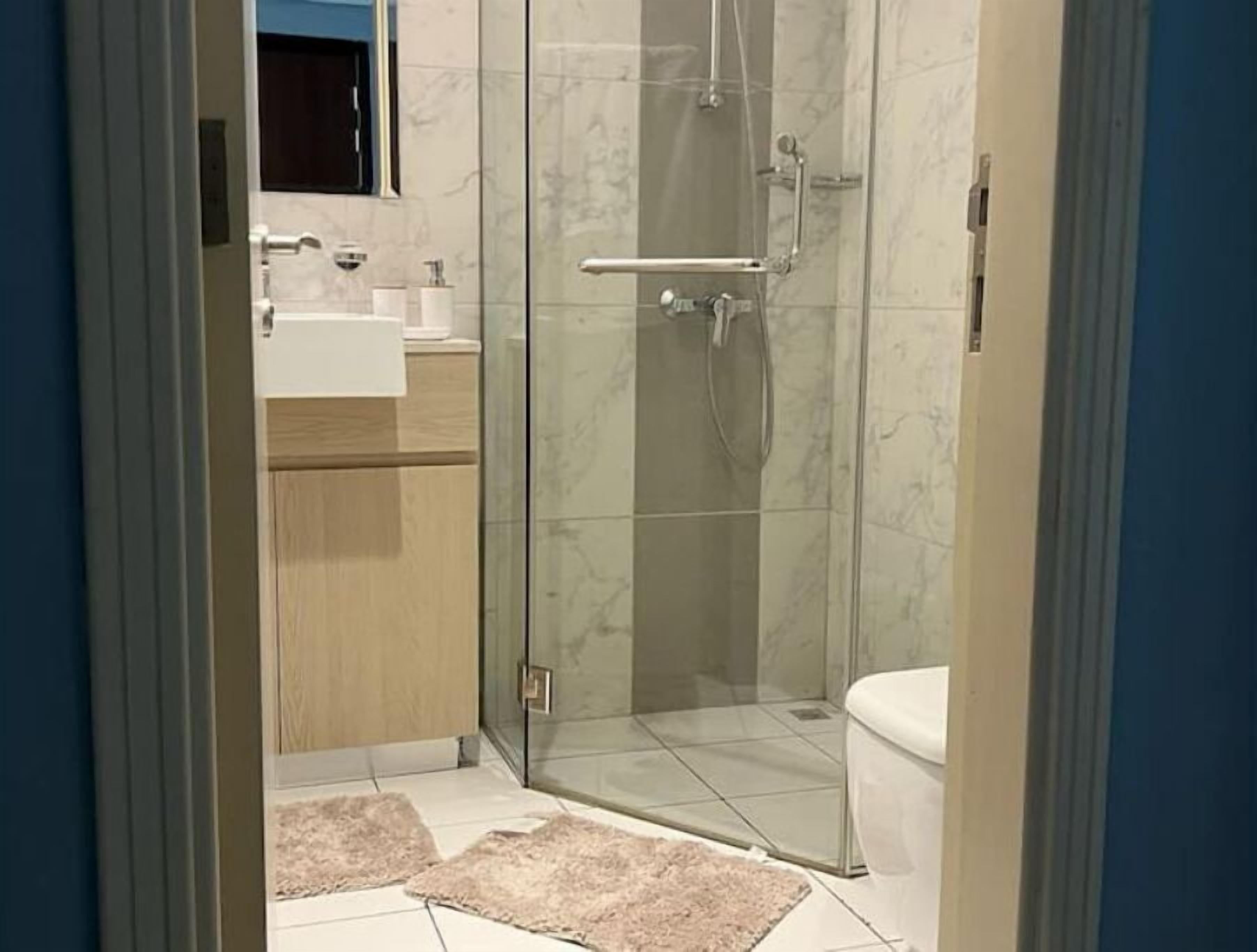 Moderni kylpyhuone, jossa on lasiseinällä varustettu suihku, wc ja peilillä varustettu pesuallas.