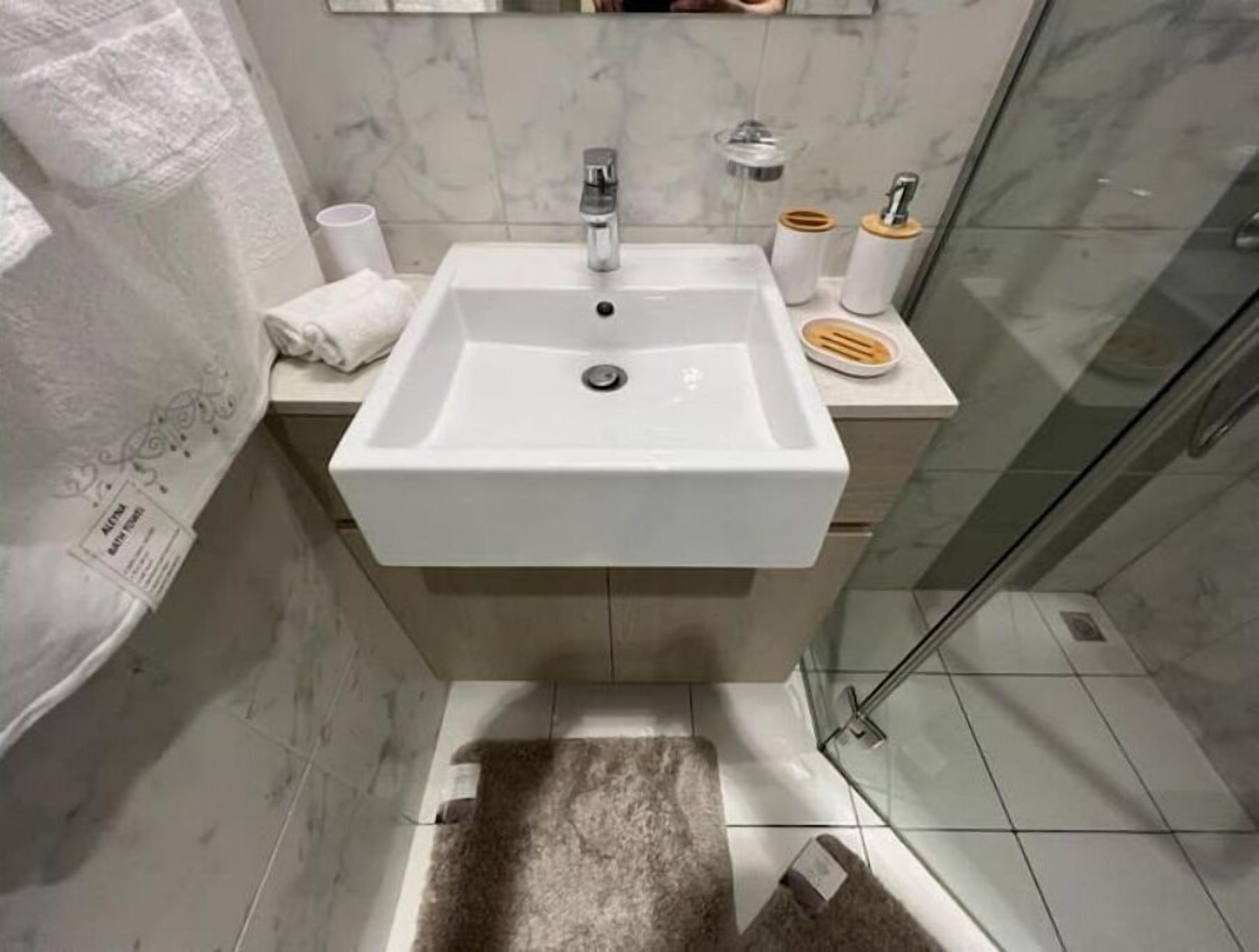 Een badkamer met een witte wastafel, een spiegel erboven en een douchegedeelte aan de rechterkant.