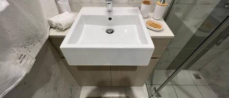 Een badkamer met een witte wastafel, een spiegel erboven en een douchegedeelte aan de rechterkant.