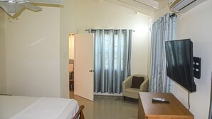 A hotel room with a bed, a desk, a chair, a television, and a curtain. - Twin Peak Cottage (Ocho Rios)