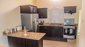 A kitchen with dark cabinets, a granite countertop, a stainless steel refrigerator, a stove, and a sink. - Twin Peak Cottage (Ocho Rios)