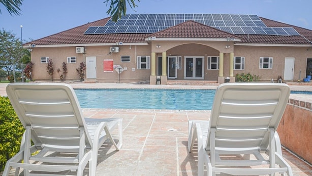 A building with a swimming pool, solar panels, and two lounge chairs. - Twin Peak Cottage (Ocho Rios)
