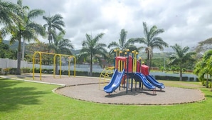 A playground with slides and swings, surrounded by grass and palm trees. - Twin Peak Cottage (Ocho Rios)