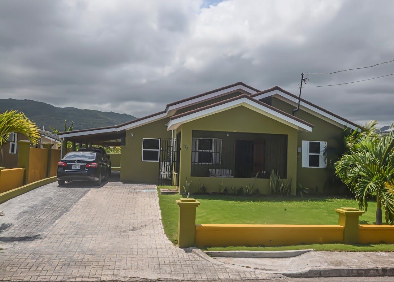 A two-story house with a paved driveway and a car parked in front.