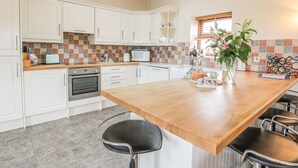 Eine moderne Küche mit weißen Schränken, einer Holzausziehtafel und einer zentralen Kochinsel mit Barhocker.