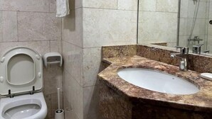 A bathroom with a toilet, a sink, a mirror, and a shower. - Studio | Steps from Downtown (Business Bay)