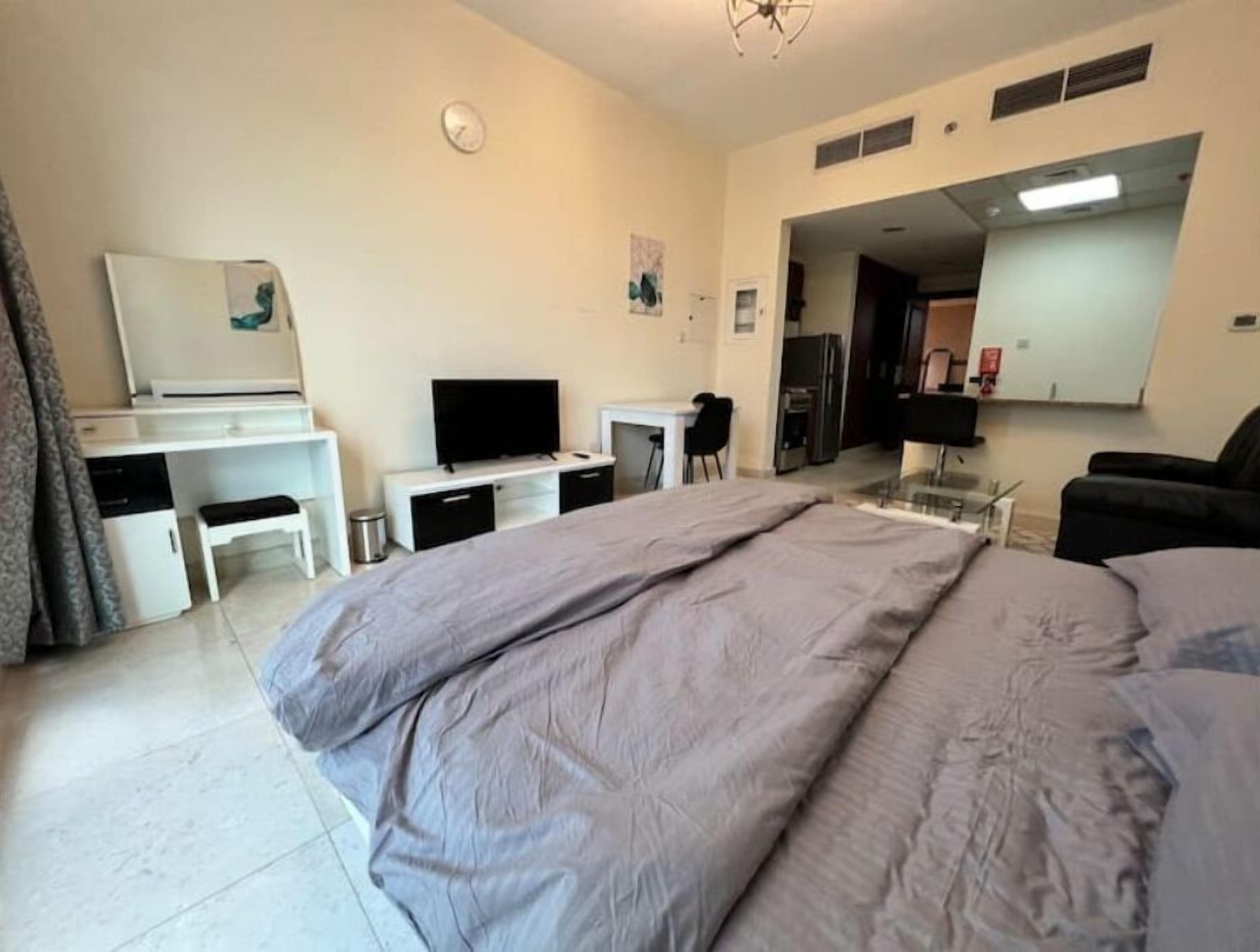 A hotel room with a bed, a desk, a chair, a television, and a small kitchenette.