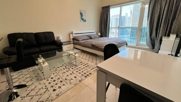A modern apartment with a bed, a sofa, a dining table, and a large window with curtains. - Studio | Steps from Downtown (Business Bay)