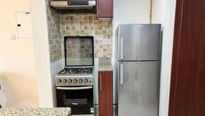 A compact kitchen with a built-in stove, oven, and a stainless steel refrigerator. - Studio | Steps from Downtown (Business Bay)