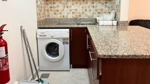 A compact kitchen with a built-in washing machine, a tiled backsplash, and granite countertops. - Studio | Steps from Downtown (Business Bay)