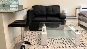 A modern living room with a black leather sofa, a glass coffee table, and a patterned rug. - Studio | Steps from Downtown (Business Bay)