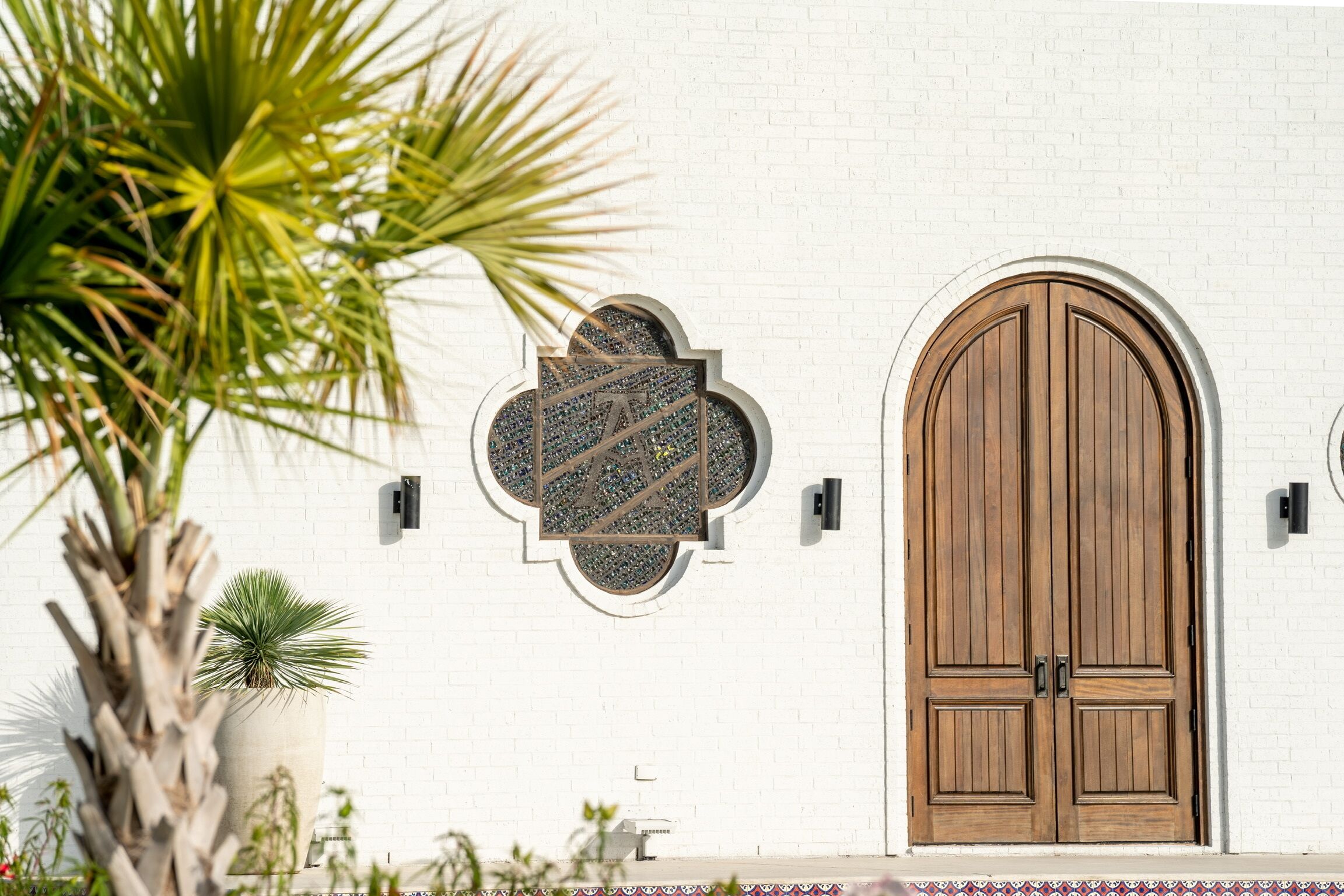 Un mur en briques blanches avec une porte en bois et un panneau de verre décoratif.