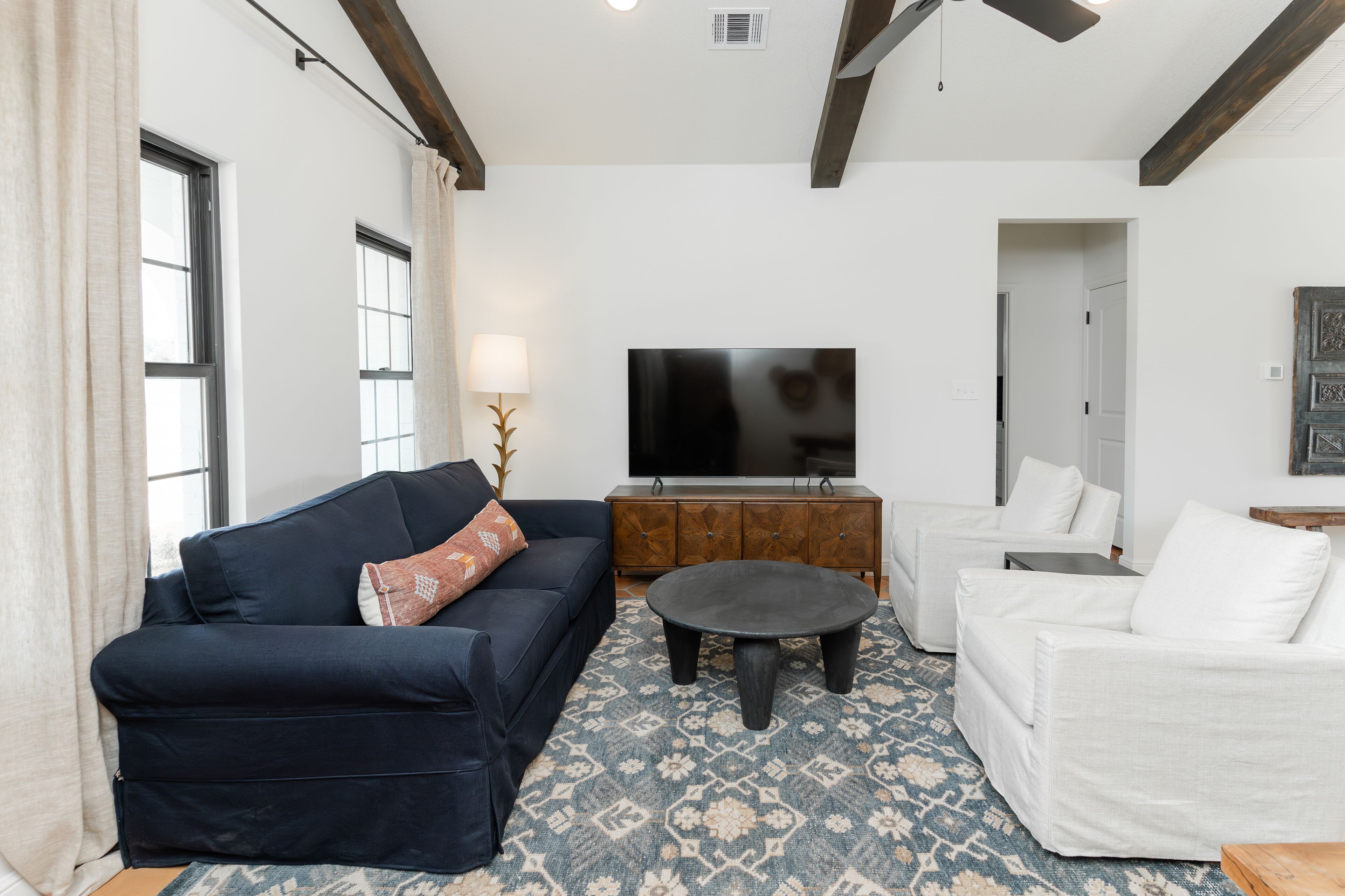 Una sala de estar con un sofá azul oscuro, un sofá blanco, una mesa de centro y un televisor sobre un mueble de madera.