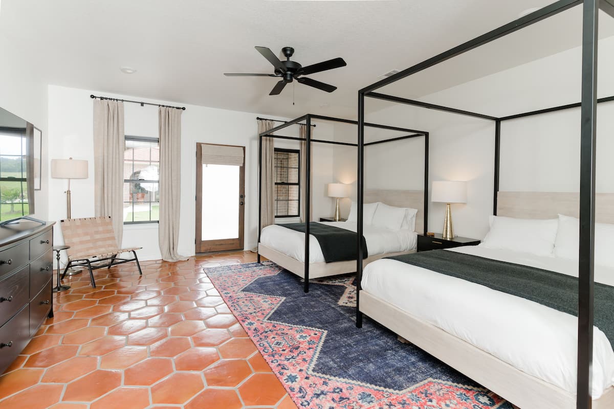 A four-poster bed with white linens, a patterned rug, and a ceiling fan.