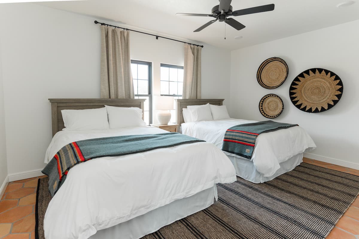 A hotel room with two beds, a ceiling fan, and a large window with curtains.