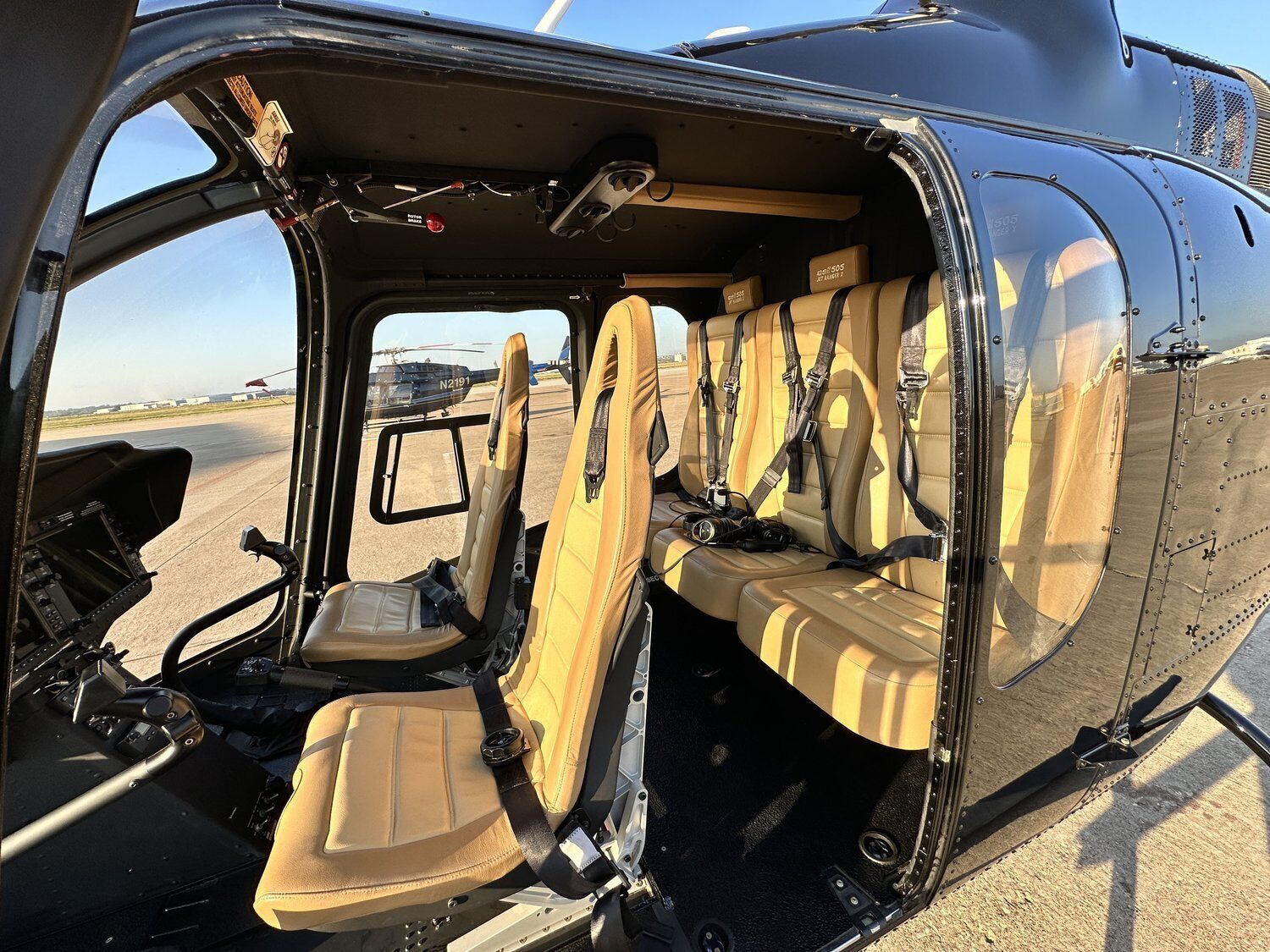 Helikopterinterieur met stoelen voorzien van veiligheidsgordels, een bedieningspaneel en helder uitzicht naar buiten.