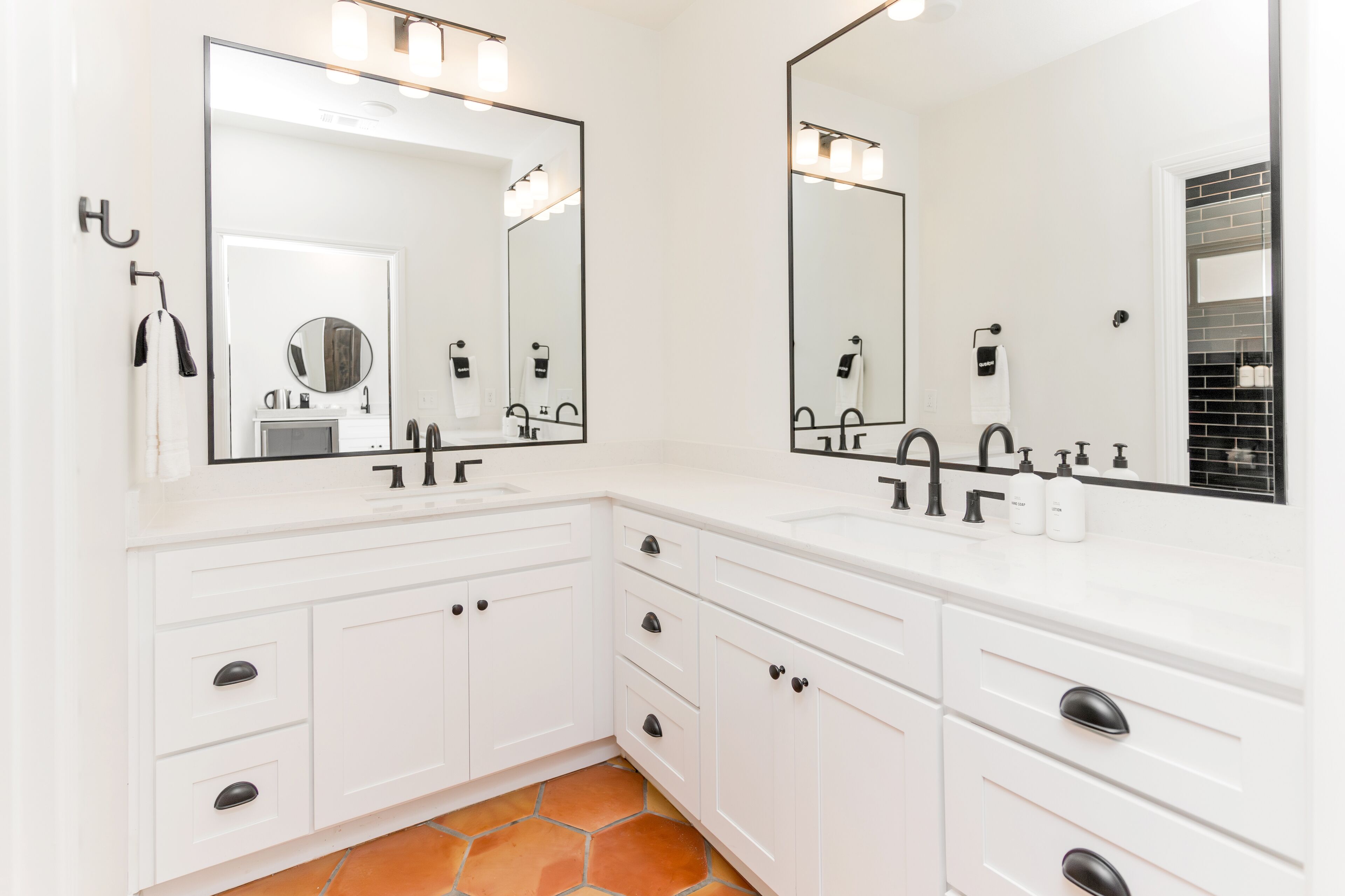 A modern bathroom with two sinks, large mirrors, and white cabinetry.