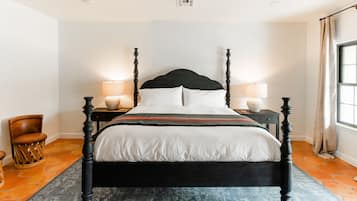 Una cama con dosel de madera oscura, ropa de cama blanca y dos lámparas de noche.