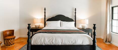 A four-poster bed with a dark wooden frame, white bedding, and two bedside lamps.