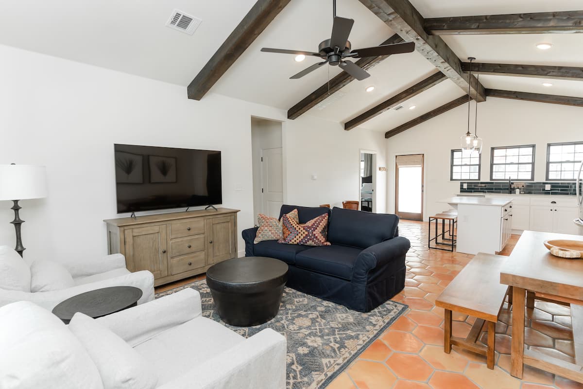 A spacious living room with a large TV, a dark blue sofa, and a wooden dining table.