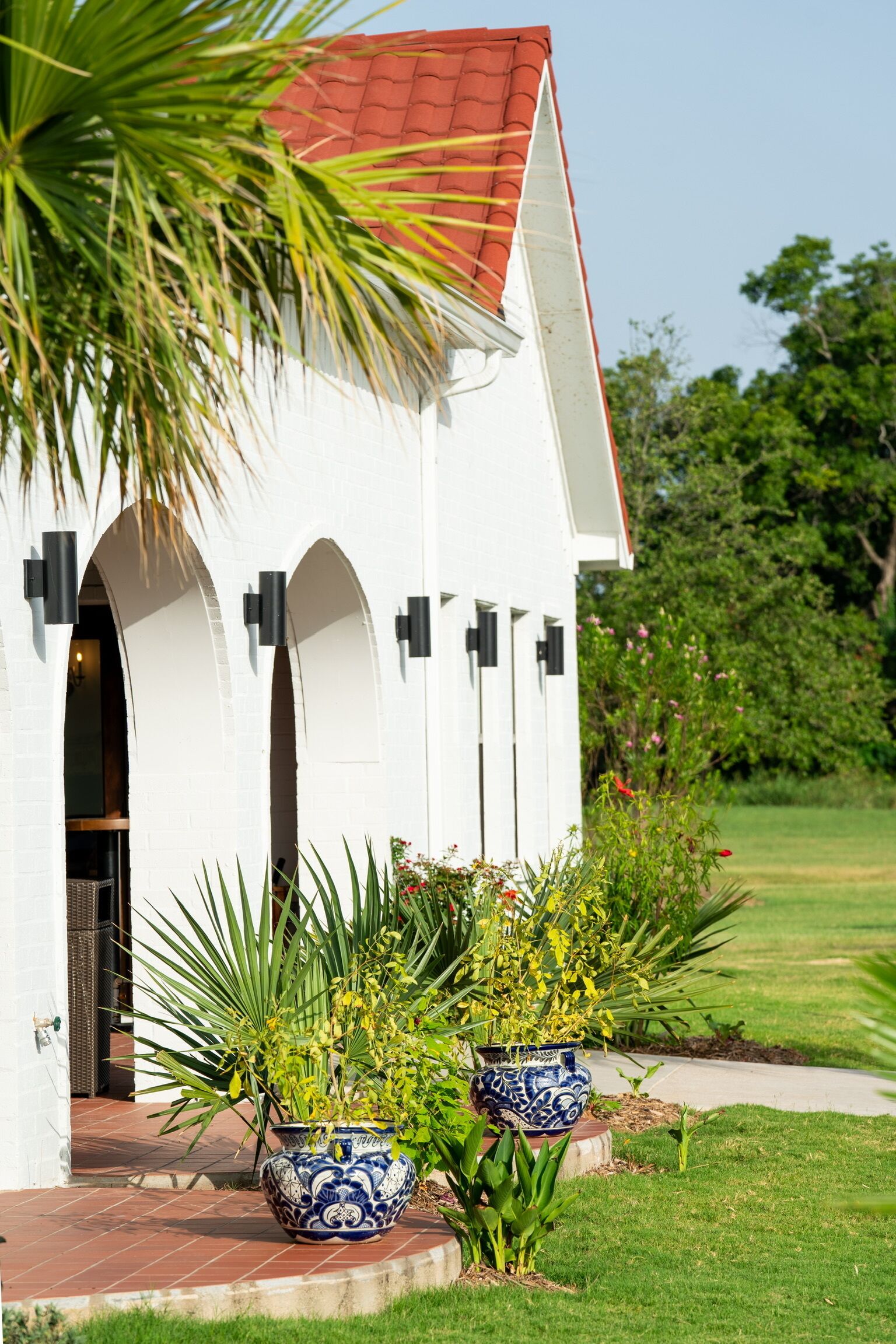 A white building with a red roof, arched doorways, and black wall-mounted lights.