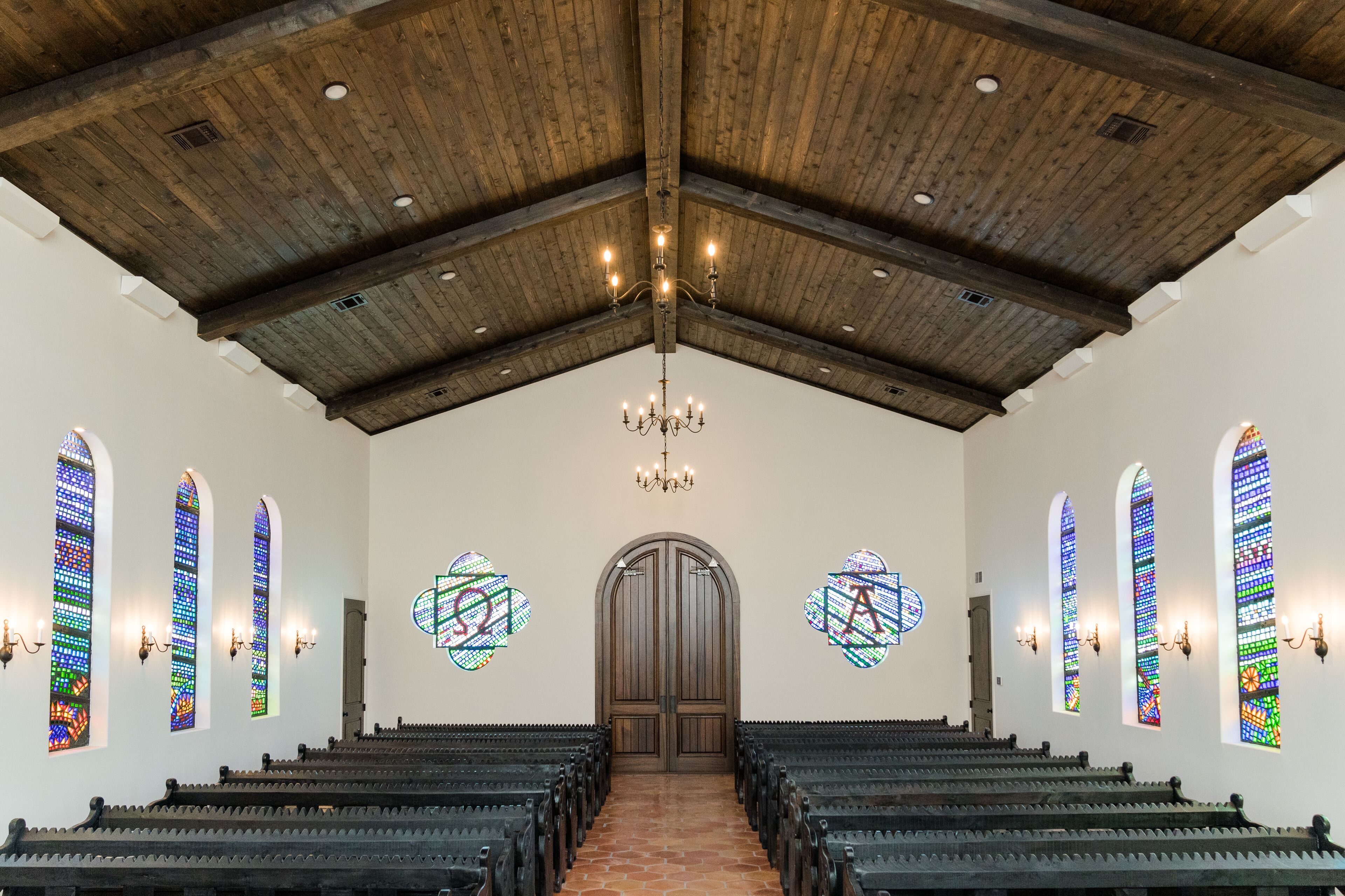 A church interior with pews, stained glass windows, and a wooden ceiling.