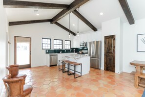 A spacious kitchen with a large island, wooden beams, and a tiled floor.