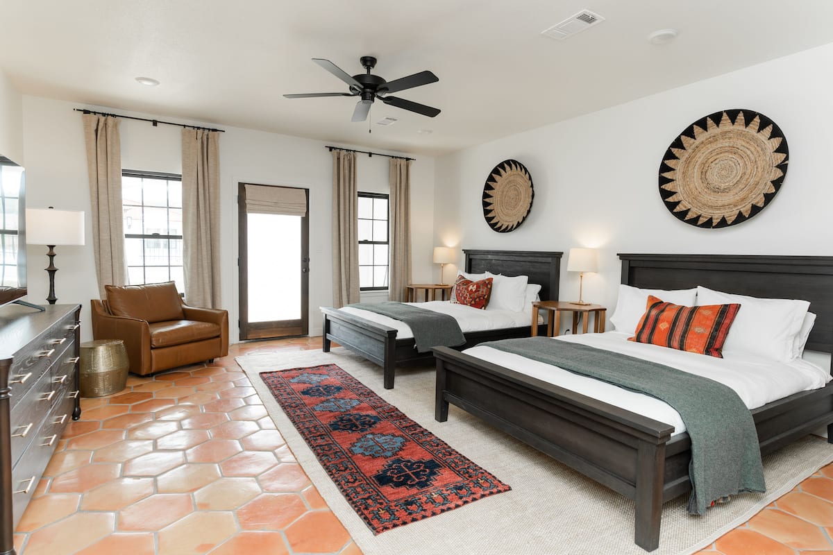 A hotel room with two beds, a ceiling fan, a large rug, and a decorative wall piece.