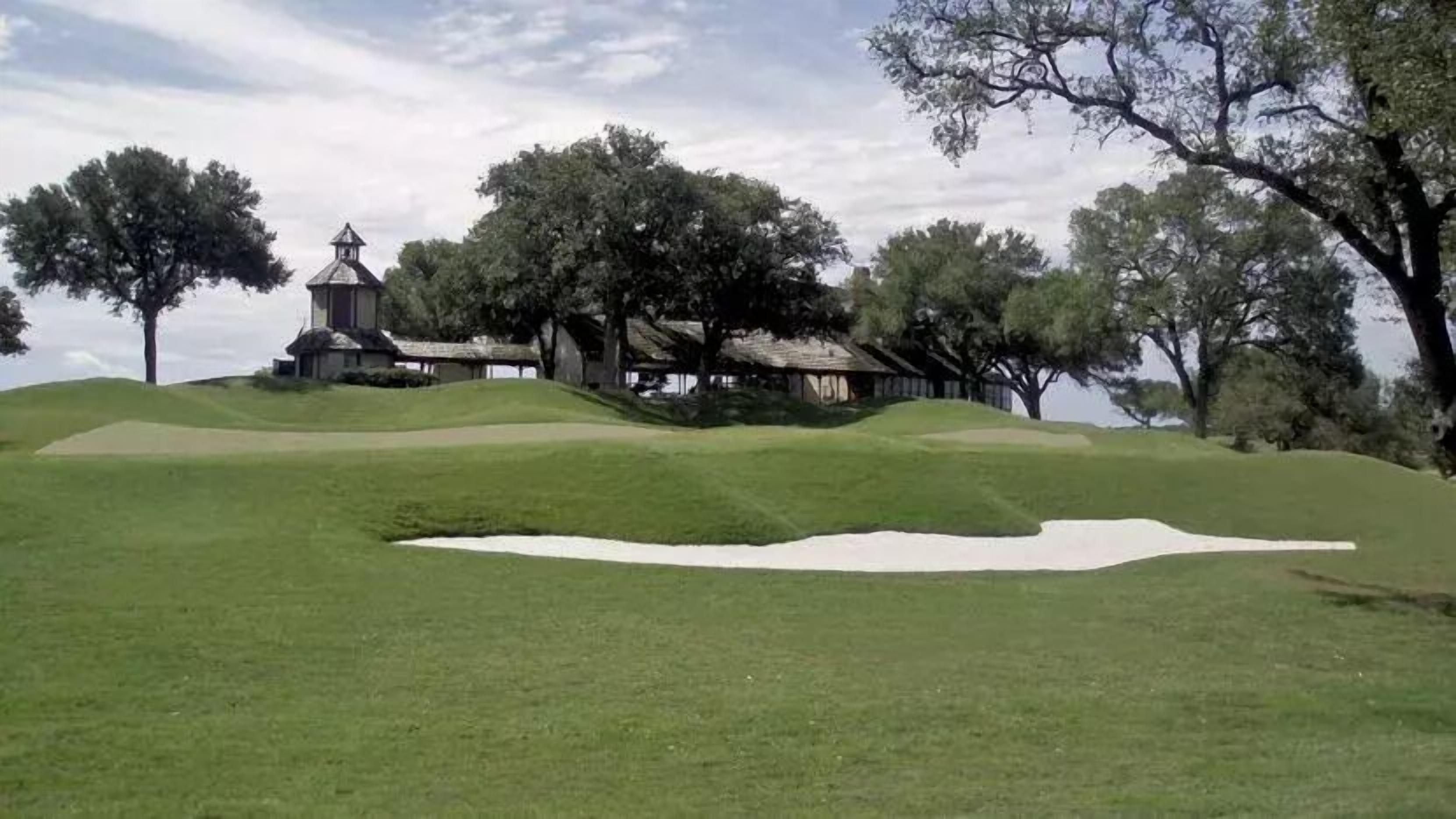 Campo de golf con búnkeres, una casa club y árboles.