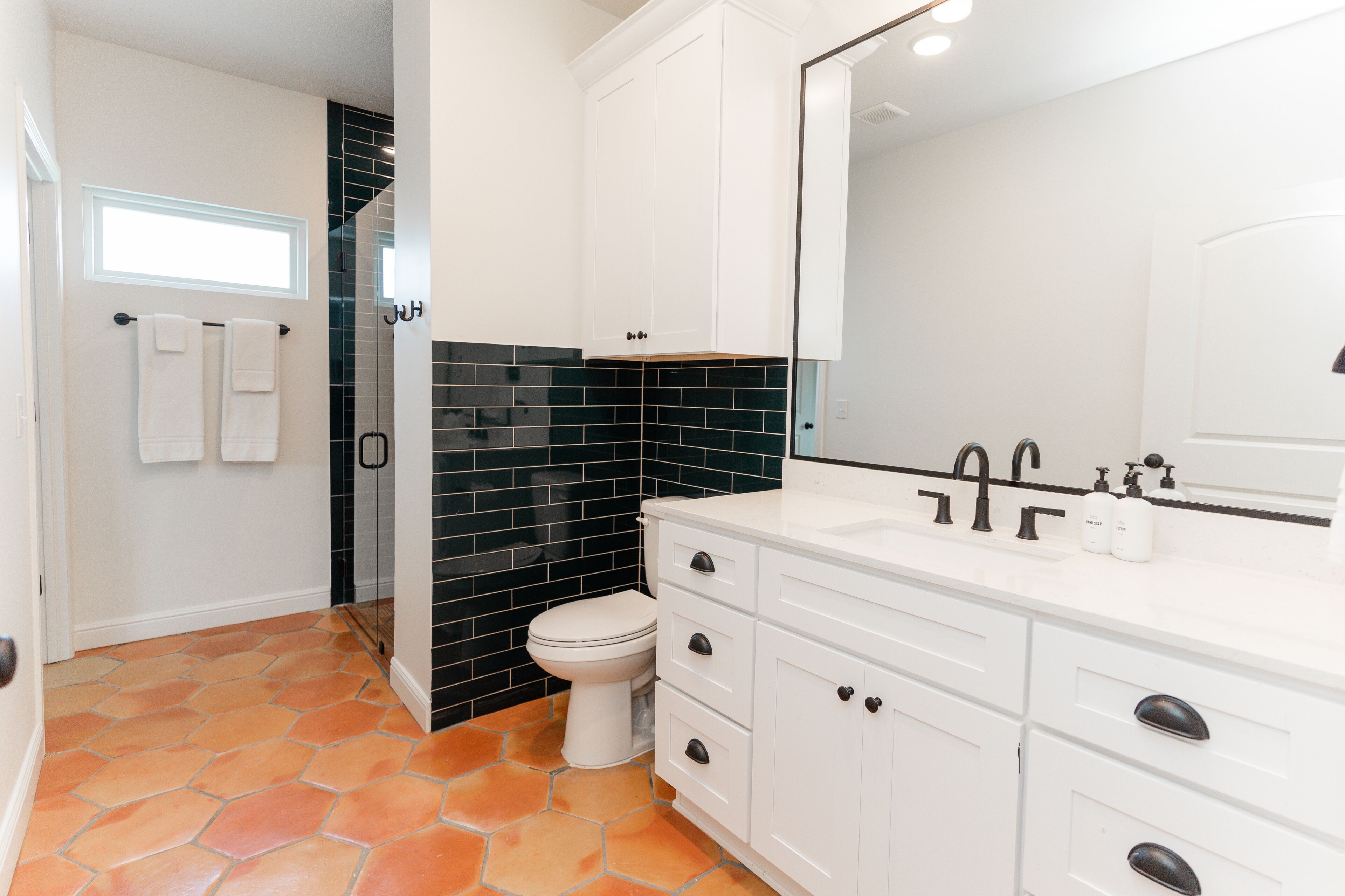 A bathroom with white cabinets, a black tiled backsplash, and a white toilet.