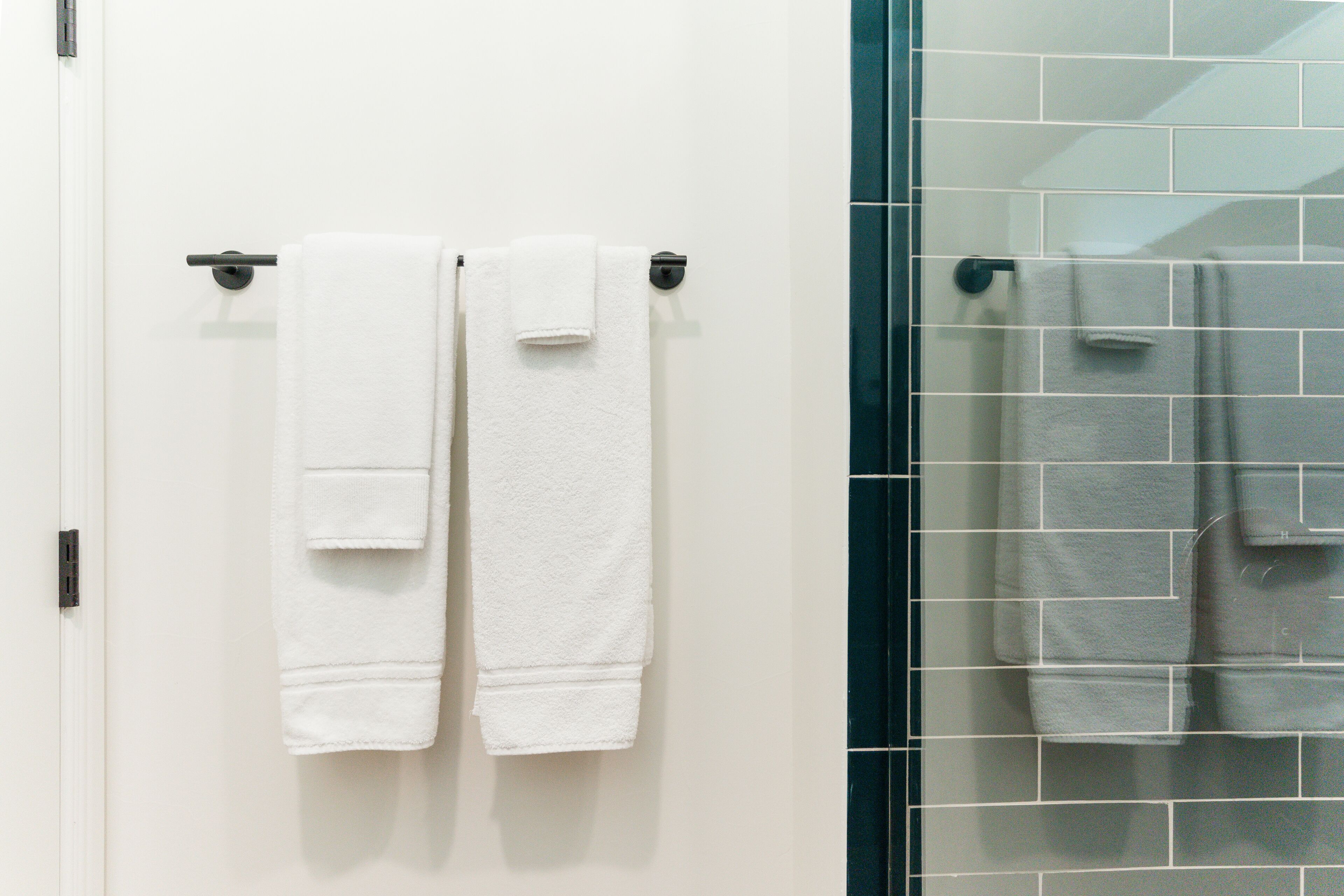A bathroom with two white towels hanging on a black towel bar, a glass shower enclosure, and a white tiled wall.