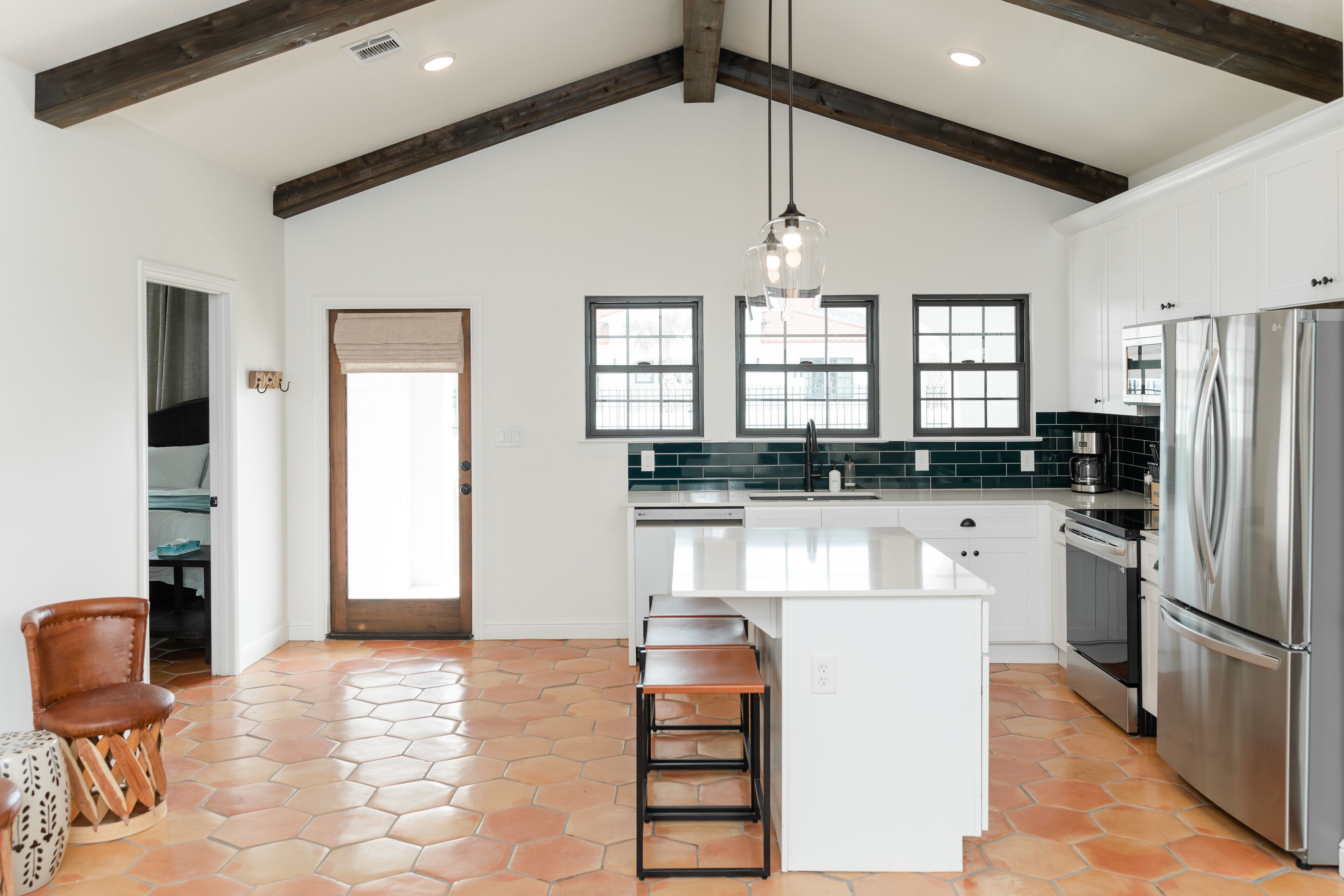 A spacious kitchen with a large island, white cabinetry, and a stainless steel refrigerator.