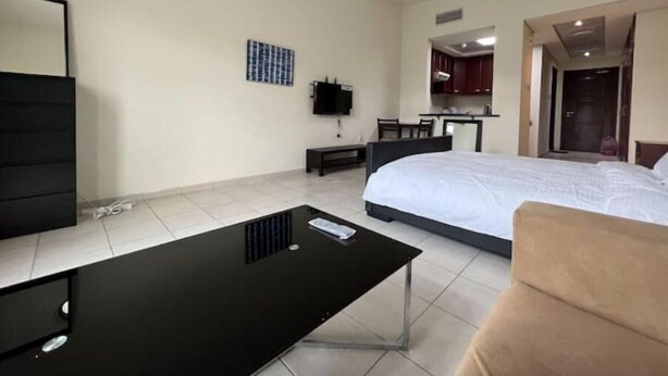 A hotel room with a bed, a black desk, a chair, a TV, and a small kitchenette.