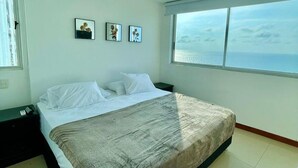 A bedroom with a bed, a nightstand, a window with a view of the sea, and three framed pictures on the wall. - 2P1-AL3 APARTAMENTO DE 2 ALC CON WIFI (Cartagena)