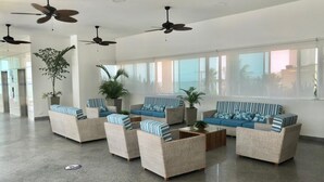 A spacious lobby with wicker furniture, ceiling fans, and large windows offering views of palm trees and buildings. - 2P1-AL3 APARTAMENTO DE 2 ALC CON WIFI (Cartagena)