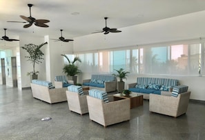 A spacious lobby with wicker furniture, ceiling fans, and large windows offering views of palm trees and buildings. - 2P1-AL3 APARTAMENTO DE 2 ALC CON WIFI (Cartagena)