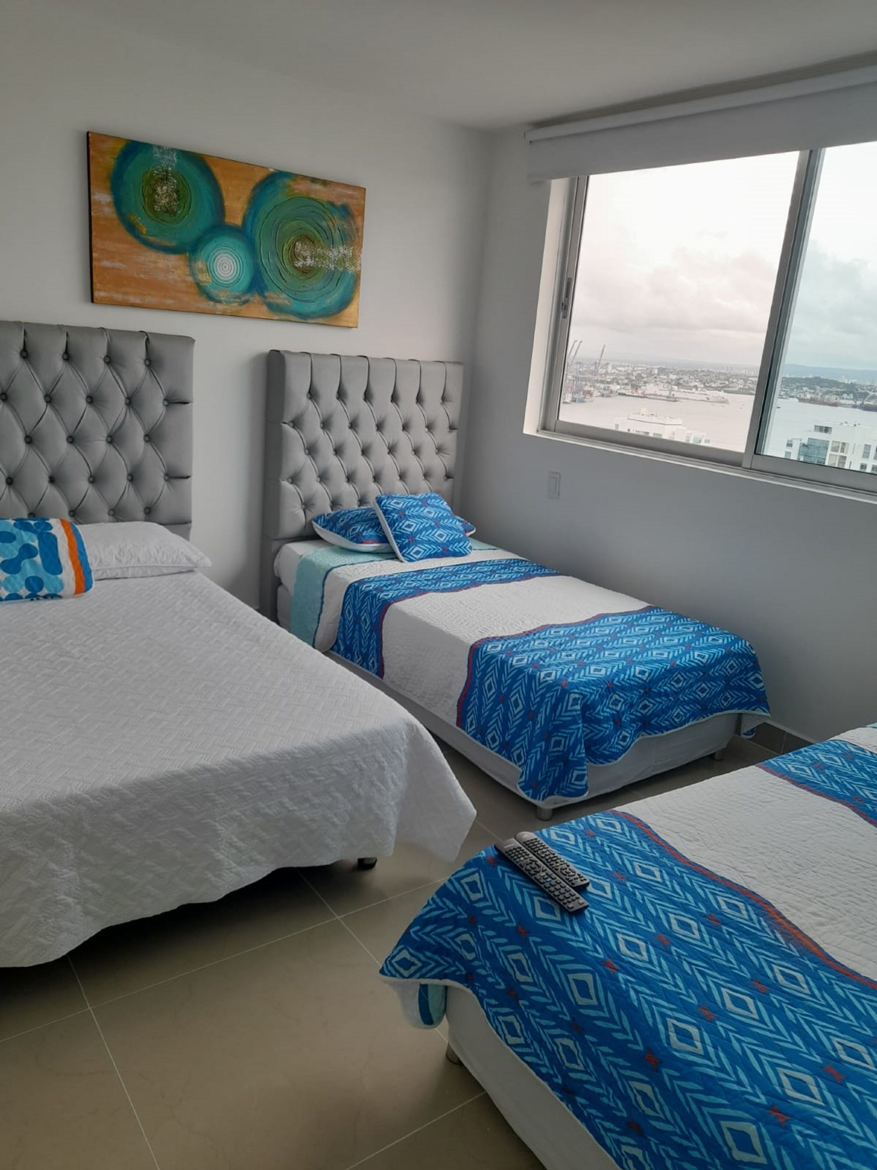 Habitación de hotel con dos camas, un ventanal con vistas a la ciudad y un cuadro en la pared.