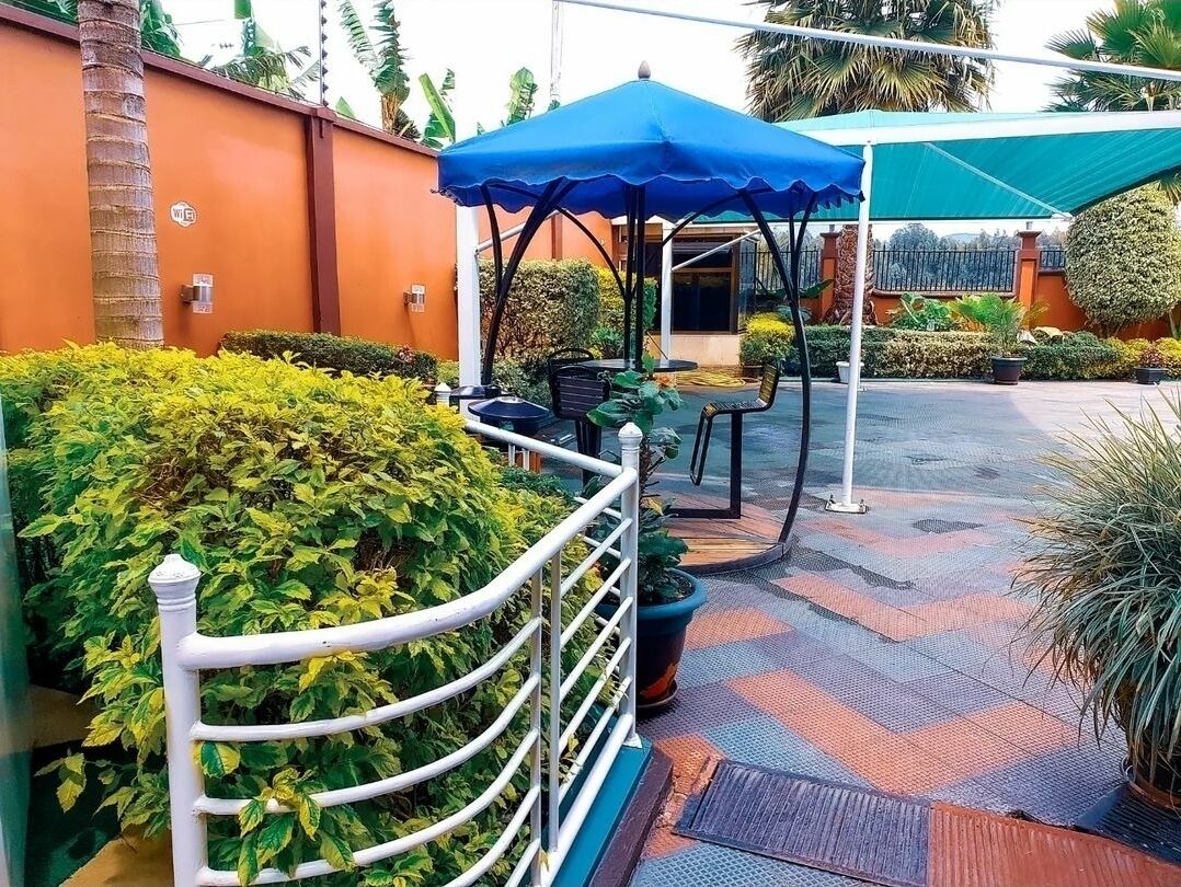 An outdoor seating area with a blue umbrella, a white fence, and potted plants.