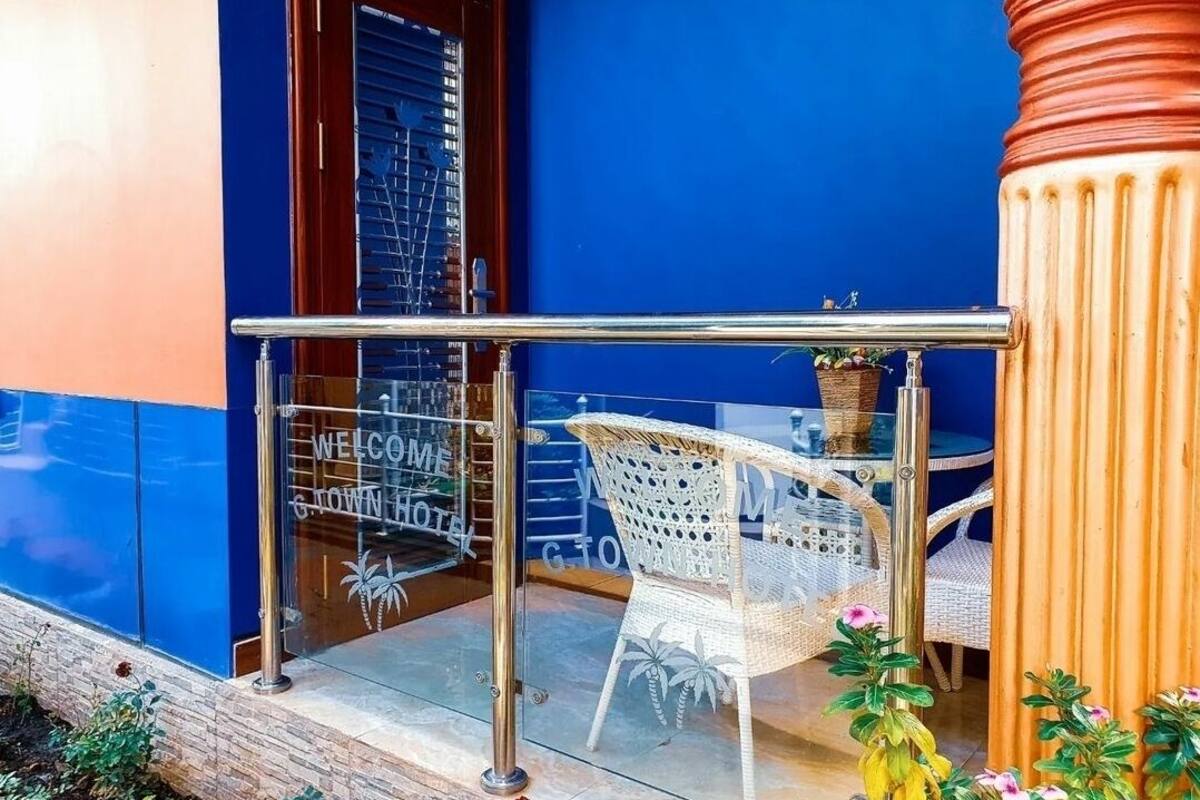 Una puerta de cristal con letreros que dicen "WELCOME" y "GOLD HOTEL", una silla de mimbre blanca y una planta en maceta.