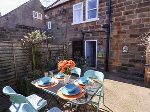 A metal table set outdoors with blue and orange plates, a vase with orange flowers, and light blue chairs. - Navigators Rest (Whitby)