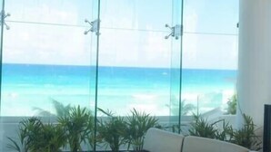 A modern interior with a glass wall offering a view of the ocean. There is a round table and a beige sofa. - STUDIO 1 AT THE BEST BEACH IN CANCUN (Cancún)
