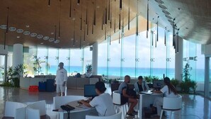 Una hall moderna di un hotel con vista sull'oceano, aree salotto e una reception.
