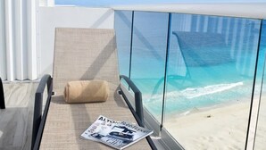 A balcony with a glass balustrade, a beige cushioned chair, and a magazine titled "Alton Robb Report". - breathtaking studio, w/ocean and lagoon views, amazing wrap around balcony,... (Cancún)