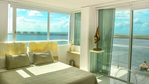 A hotel room with a large bed, a nightstand, a lamp, and a view of the ocean through large windows. - breathtaking studio, w/ocean and lagoon views, amazing wrap around balcony,... (Cancún)