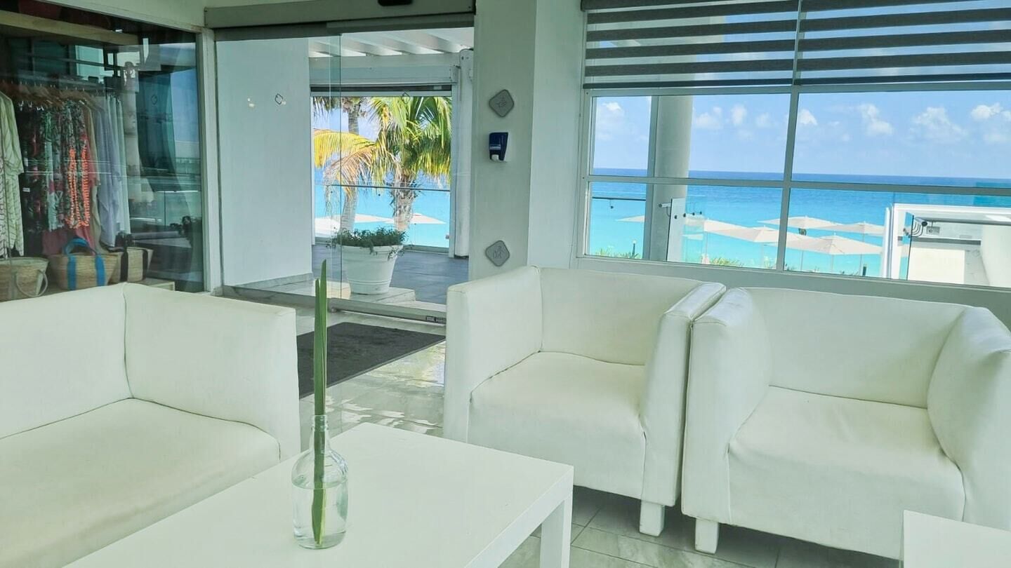 Um hall de hotel moderno, com sofás brancos e uma janela ampla com vista para a praia e o oceano.